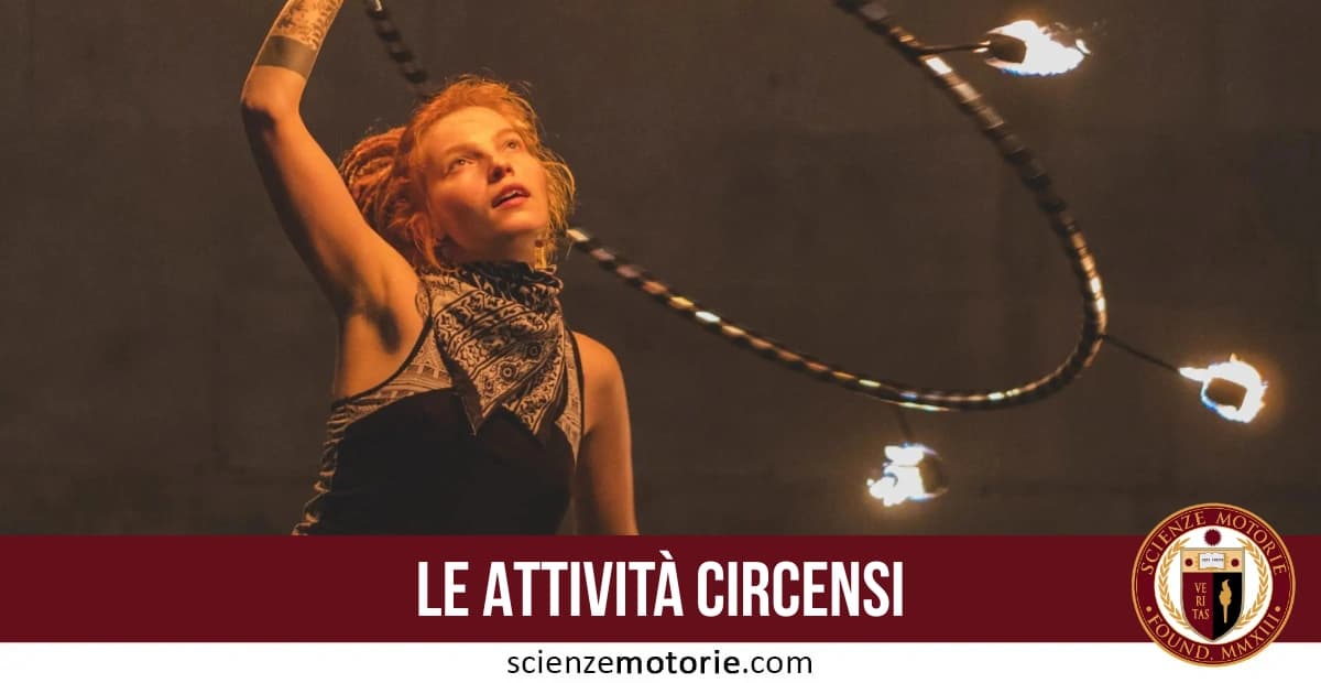 Performer circense con top scuro e fazzoletto al collo manipola attrezzo con fiamme, con la scritta “LE ATTIVITÀ CIRCENSI” e il logo di scienzemotorie.com in basso.