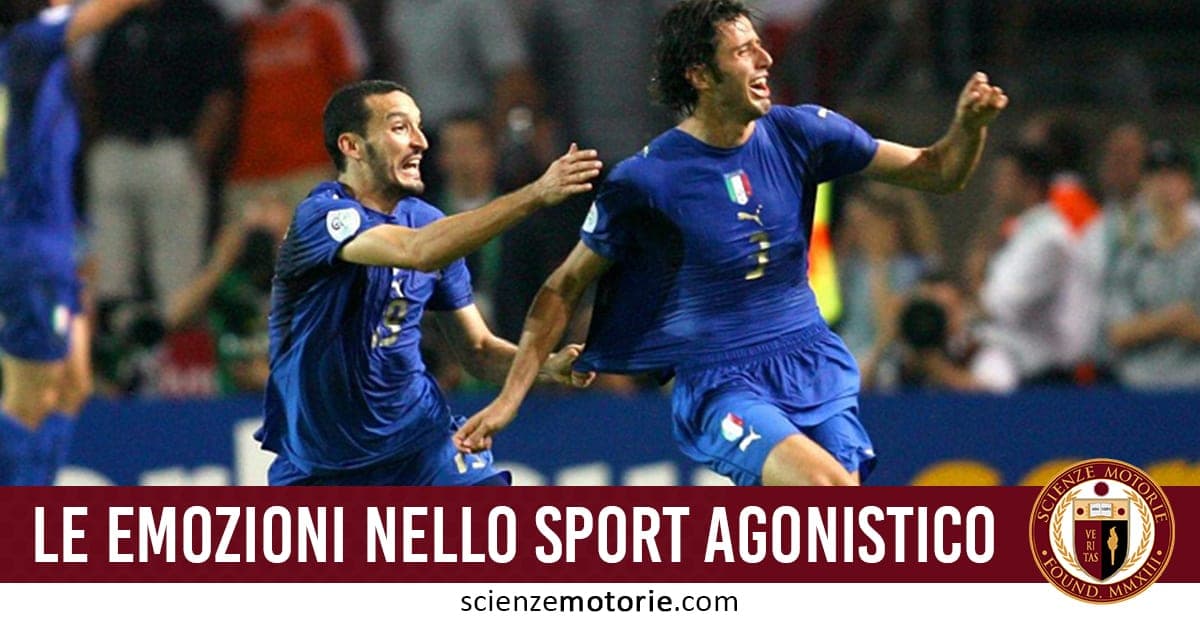 Due calciatori in divisa blu esultano in campo durante una partita di calcio, con spettatori sfocati sullo sfondo.