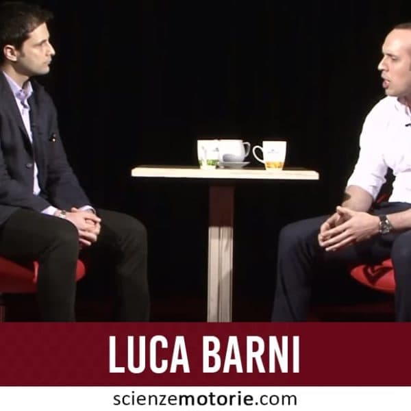 Due uomini vestiti formalmente seduti su sedie rosse di fronte a un tavolo con tazze, con sfondo scuro; Luca Barni.