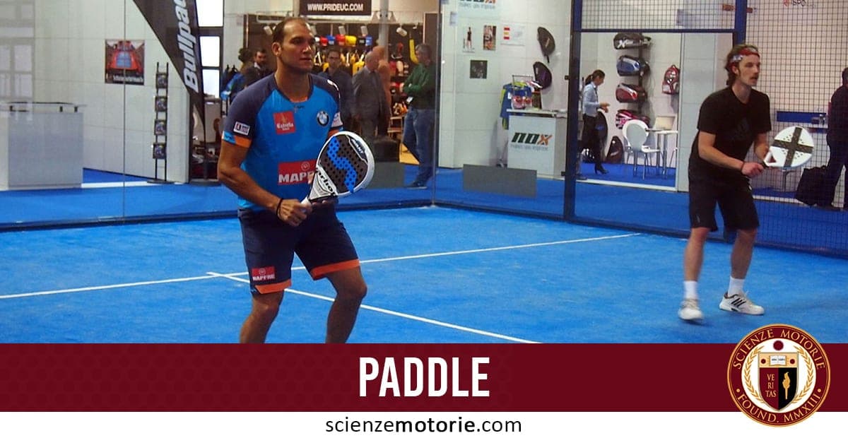 Due giocatori su un campo da paddle con pavimento blu e pareti di vetro, pronti a giocare con le loro racchette.