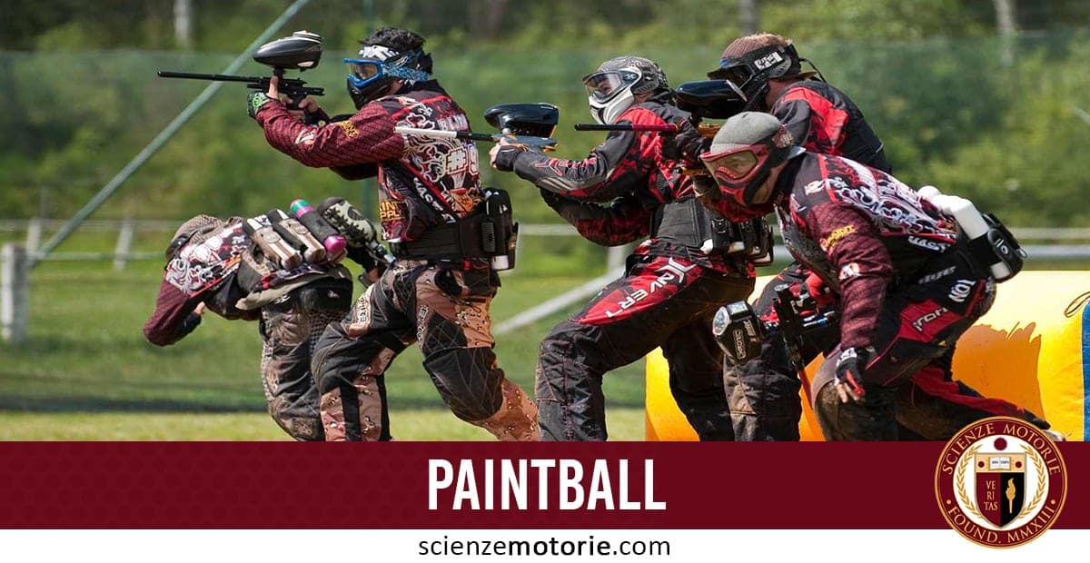 Gruppo di giocatori di paintball con maschere protettive e fucili da paintball in un campo all'aperto con ostacoli.