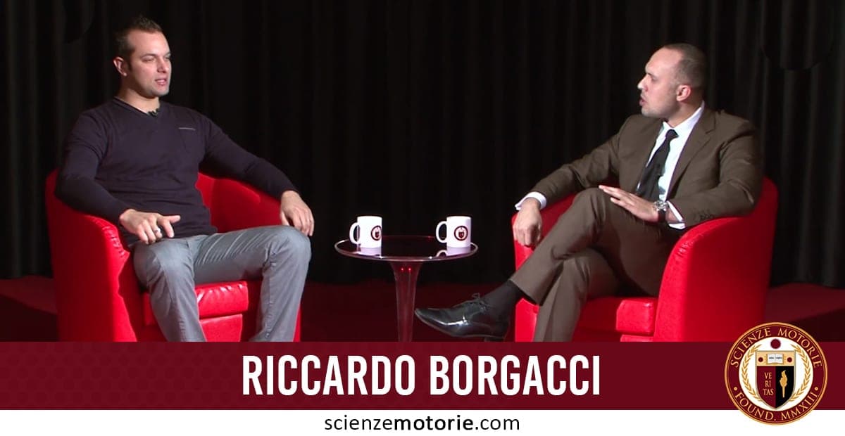 Foto di Riccardo Borgacci con maglione scuro e Giacomo Catalani in abito marrone e cravatta durante un’intervista per Scienze Motorie.