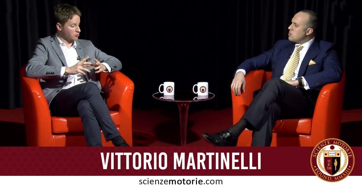 Vittorio Martinelli (a sinistra) e Giacomo Catalani (a destra) seduti su poltrone rosse durante una conversazione. Entrambi indossano abiti formali. Tra loro un tavolino con due tazze. Sullo sfondo, una tenda nera. In basso si legge "Vittorio Martinelli" e il logo di Scienze Motorie.