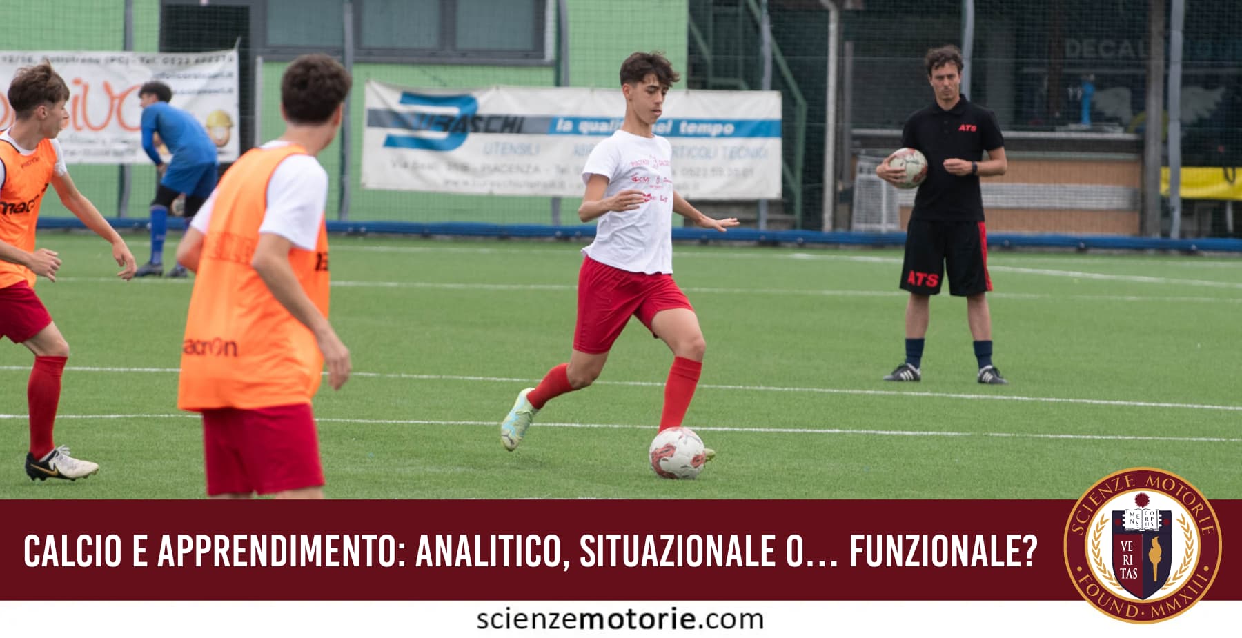 Allenamento di calcio giovanile su campo sintetico con esercitazione di conduzione palla e osservazione dell’allenatore